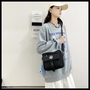 Detail of black crossbody bag featuring buckle flap and a blue cartoon keychain accessory
