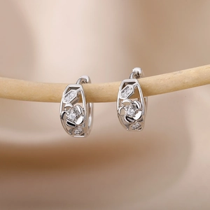 Close-up of silver C-shaped zircon earrings with hollow flower design on a silk background