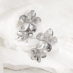 Detail of silver double floral earrings with textured metallic finish on a white stone base