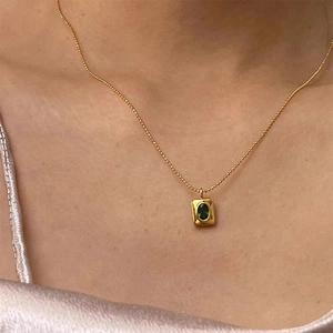 Close-up of a gold square pendant necklace featuring a green oval gemstone on a model