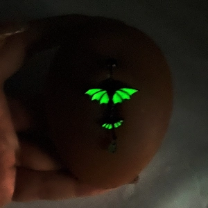 Luminous bat navel piercing with glowing green wings shown in a dark environment