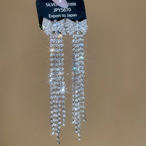 Macro view of silver bow earrings with long sparkling rhinestone tassels on black card