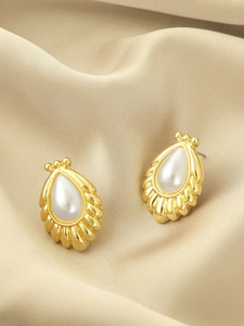 Macro shot of elegant drop-shaped gold earrings with baroque pearls on champagne silk fabric