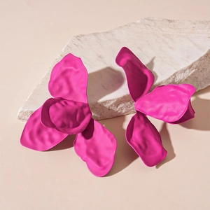 Macro detail of vibrant rose red pleated flower petal earrings on a stone display