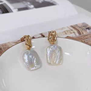 Dettaglio di orecchini con perle barocche e metallo dorato testurizzato su piatto ceramica