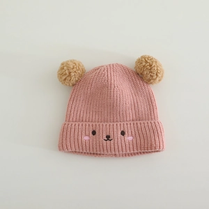 Detailed knit texture of pink baby winter hat with double brown pom-poms and cute bear face
