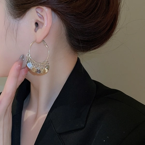 Detail view of large gold hoop earrings with layered metal sequins on a side-profile model