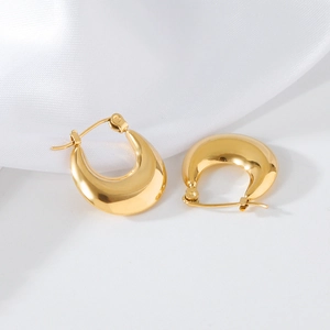 Macro shot of polished gold-plated irregular curved hoop earrings on white silk fabric
