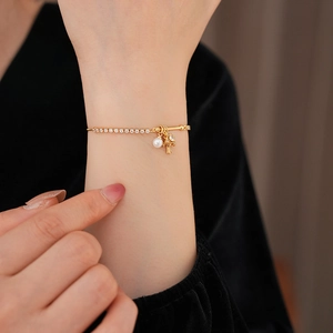 Detail of gold bracelet featuring zircon stones, a white pearl and a floral charm on wrist