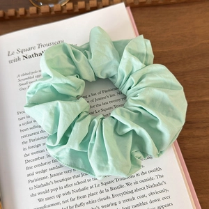 Close-up of light green fabric scrunchie on vintage book pages with soft textures