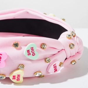 Close-up of pink fabric headband with sparkly gold rhinestones and HUG ME candy hearts