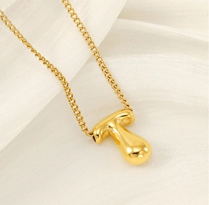 Close-up of golden bubble initial necklace on silk fabric showing shiny metal texture