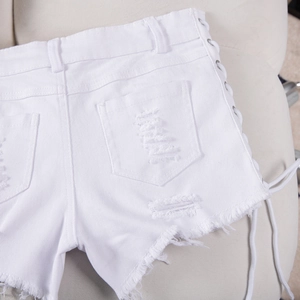Dettaglio degli shorts in denim bianco strappato con lacci e occhielli in metallo sul retro