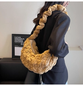 Detail of a large yellow pleated cloud bag with quilted velvet texture worn by a model