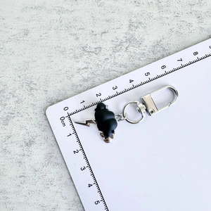 Detailed view of 3cm black cloud keychain with silver lightning on a measuring ruler