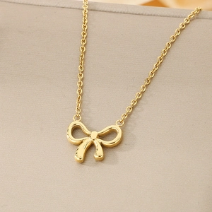 Close-up of minimalist gold bow necklace displayed on a gray jewelry box