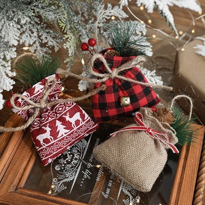 Three Christmas burlap gift bags with elk patterns and pine cone decor on wood tray