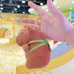 Plush capybara keychain with green mini bag accessory on golden metal hook