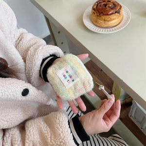 Close-up of a mini plush rainbow makeup bag held by hand in a cozy cafe setting