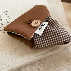 Close-up of brown plaid fabric pouch with buttons and bow detail on a vintage book