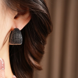 Close-up of elegant black cubic zirconia C-shape hoop earrings on model with warm lighting