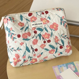 Detail of floral quilted makeup bag featuring cherry patterns and a woven logo label