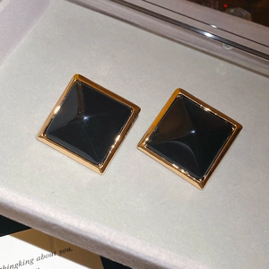 Vue macro de boucles d'oreilles carrées dorées avec résine noire en pyramide dans un écrin