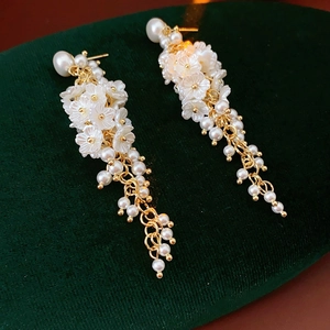 Close-up of pearl flower earrings with gold tassels on a dark green velvet stand
