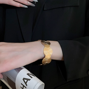 Detail of gold geometric open bangle with spiral texture shown on a black blazer sleeve