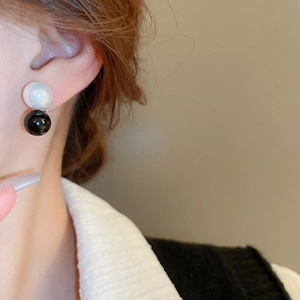 Close-up of black and white geometric faux pearl stud earrings worn on ear for daily style