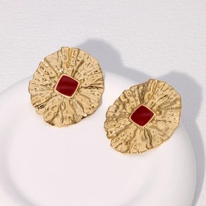 Macro shot of vintage gold earrings with irregular texture and red square enamel detail