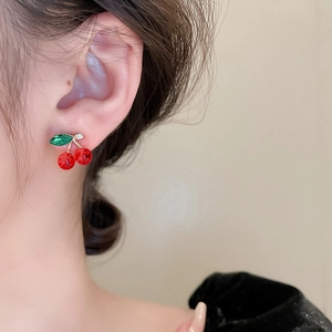 Elegant red cherry stud earrings with green crystal leaves worn by a female model