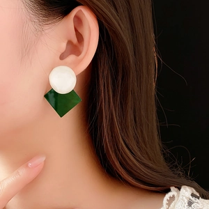 Close-up of geometric resin earrings with white round studs and green diamond pendants