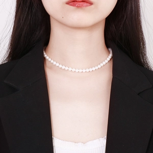 Close-up of a classic white pearl choker necklace worn by a model in a black suit
