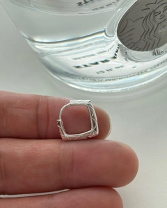 Detail of silver geometric quilted earrings held by hand showing faceted metal texture