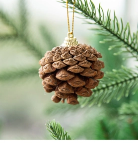 Close-up of a natural pine cone ornament with golden string hanging on a green tree