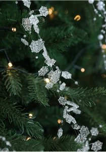 Close-up of crystal snowflake ornaments with warm lights on a green Christmas tree