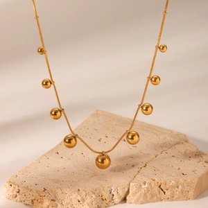 Golden stainless steel snake chain necklace with multiple beads on a textured stone