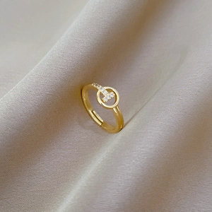 Detail of gold-plated T-letter ring with sparkling zircons on elegant champagne silk