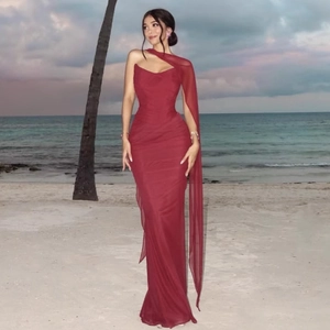 Elegant burgundy one-shoulder evening dress with flowing chiffon cape on a scenic beach