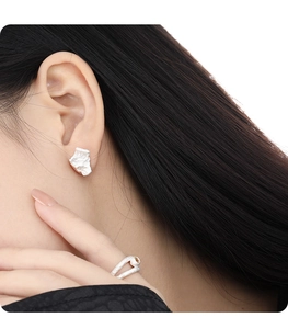 Macro shot of silver stud earrings with unique irregular pleated metal texture and finish