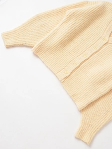Détail du gilet en maille crème avec motif à côtes verticales et petits boutons