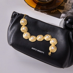 Detailed view of a gold bracelet with white pearls and spiral texture on black leather