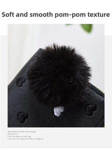 Detail of mini leather purse showing embroidered hearts and a soft black plush pom-pom