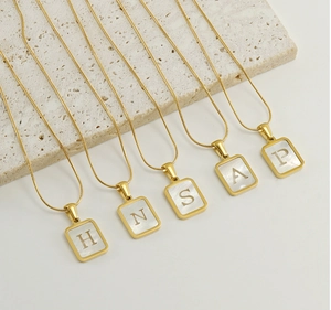 Macro view of gold plated necklaces with rectangle white shell letter pendants H N S A P