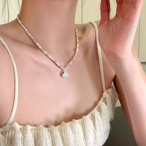 Detail of silver clover pendant and white pearl necklace worn on model for an elegant look