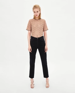 Dettaglio di un top in pizzo beige con bordi neri ondulati e motivi traforati fini