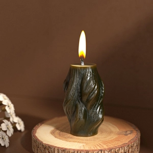 Close-up of a lit dark green wavy column candle on a wooden base with a warm atmosphere