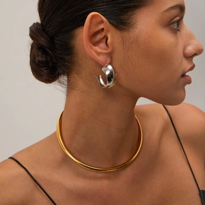 Close-up of model wearing two-tone gold and silver C-shaped hoop earrings and gold necklace