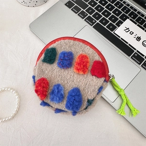 Close-up of beige plush round pouch with colorful decorative pom-poms and red zipper